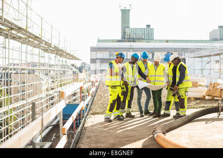 Architects and construction workers analyzing blueprint together at site Stock Photo
