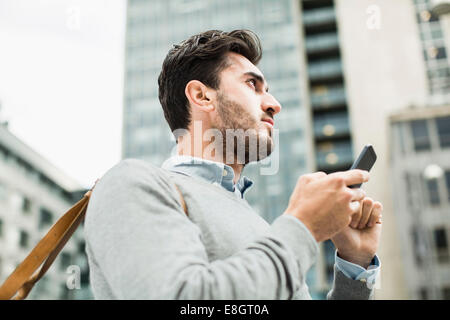 Low angle view of businessman looking away while holding smart phone against building Stock Photo