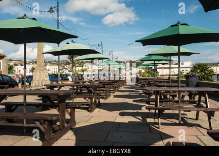 The sea front promenade at Teignmouth in Devon. Outside dining tables and benches with large green umbrellas over them. Stock Photo