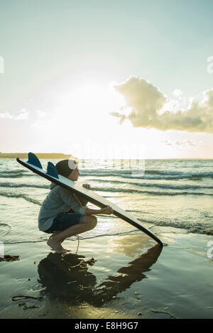 Teenage boy crouching at waterside of the sea with hir surfboard Stock Photo