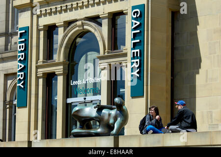 Leeds, UK. Young couple relaxing next to the Henry Moore sculpture 'Reclining Woman' outside the Leeds Art Gallery, The Headrow. Stock Photo