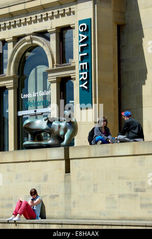 Leeds, UK. People relaxing in the sun next to the Henry Moore sculpture 'Reclining Woman' outside the Leeds Art Gallery. Stock Photo