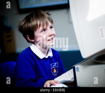 Portrait of a happy schoolboy in a class using a desktop computer with a mouse Stock Photo