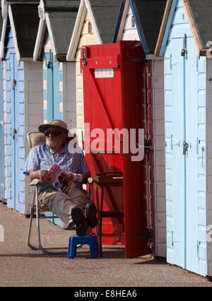 Old man sat outside beach hut, Seaton, Devon, UK Stock Photo