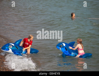 Two girls playing in the sea on inflatable dolphins Stock Photo