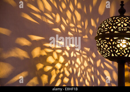 Horizontal close up of a traditional metal lampshade casting shadows on a wall in the souks of Marrakech. Stock Photo
