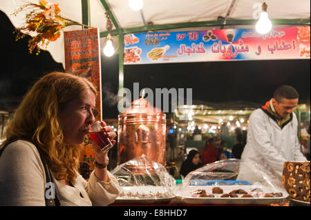 Horizontal portrait of a tourist drinking mint tea at a stall in Place Jemaa el Fna (Djemaa el Fnaa) in Marrakech at night Stock Photo