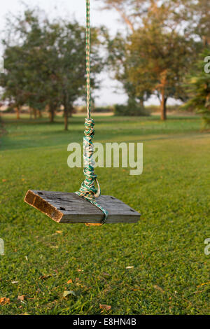 A child's rope swing hanging from a tree in a garden hangs unused, seemingly abandoned Stock Photo