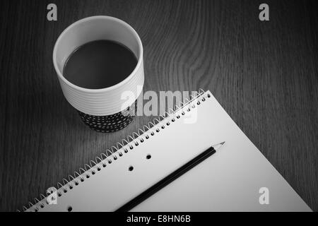 Coffee with milk in coffee cup by white paper and pencil on desk in black and white Stock Photo