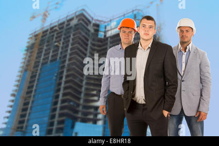 Group of three engineers and architects in their hardhats standing grouped in front of a skyscraper under construction on a building site in a teamwork and professional careers concept. Stock Photo