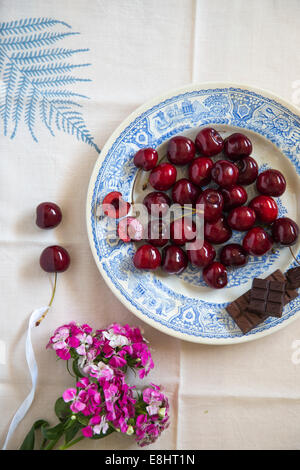 whole cherries and chocolate on blue ceramic plate, with leaf motif table linen and flowers