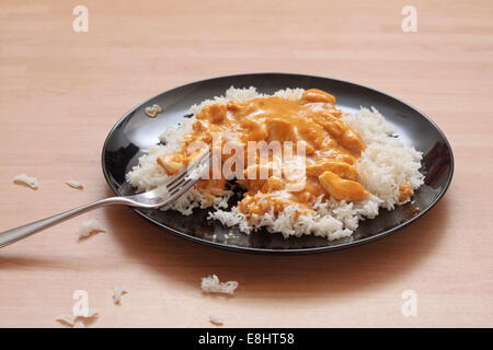 A plate of chicken korma and rice on a black plate with dropped rice around plate on table Stock Photo