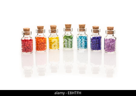 Tiny glass bottles with a cork stopper, filled with a rainbow colours of beads, on a white background Stock Photo
