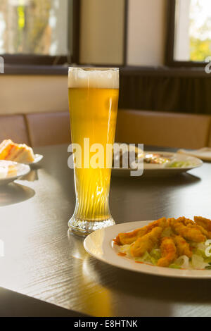 Tall Glass of Beer on Restaurant Table with Plated Food Dishes Stock Photo