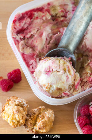 homemade white chocolate ice cream with raspberry ripple and almond cookie pieces, in container with scoop. Stock Photo