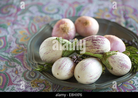 plated white aubergines with purple fine stripes and onion against purple floral tablecloth, text space, Stock Photo