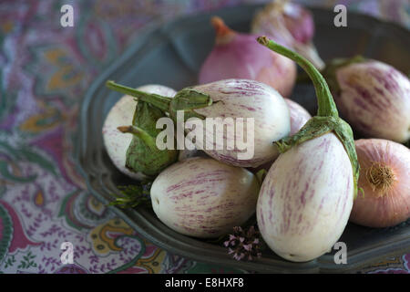 close up of plated white aubergines with purple fine stripes against purple floral tablecloth Stock Photo