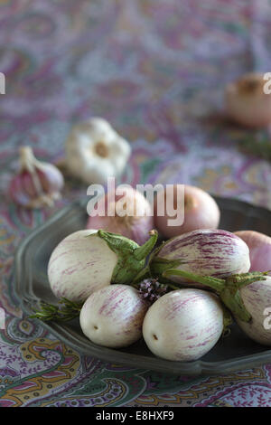 plated white aubergines with purple fine stripes, onion and garlic against purple floral tablecloth Stock Photo