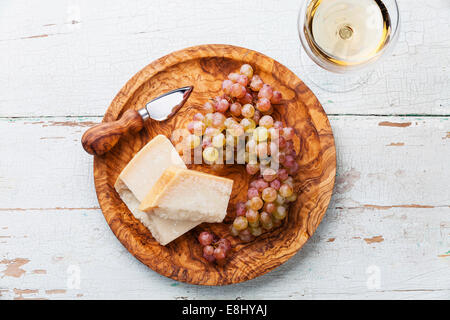 Parmesan cheese and kishmish grapes on olive wood plate and wine Stock Photo