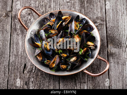 Boiled mussels in copper cooking dish on dark wooden background