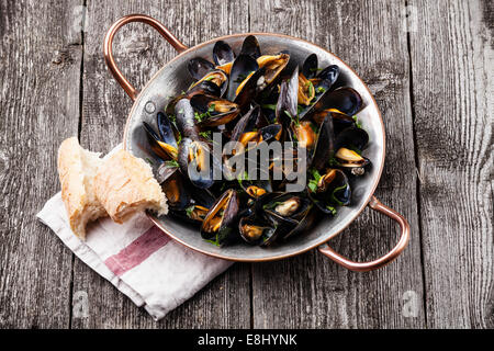 Mussels in copper cooking dish and French Baguette on dark wooden background