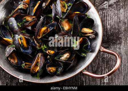 Boiled mussels in copper cooking dish on dark wooden background close up