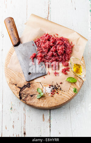 Raw chopped meat and meat cleaver on wooden cutting board on blue background Stock Photo