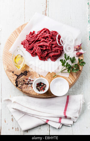Fresh minced meat with onion and spices on wooden cutting board on blue background Stock Photo