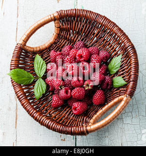 Raspberries with leaves in basket on blue background Stock Photo