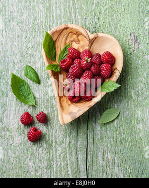 Raspberries with leaves in olive wood bowl shape of heart on green wooden background Stock Photo
