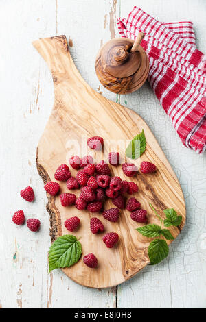 Raspberries with leaves on olive wood cutting board on blue textured background Stock Photo
