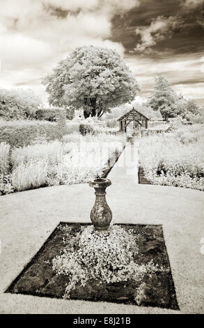 Infrared photograph of a classic English garden ornate sundial feature on lawn with borders of herbaceous perennials at Wollerto Stock Photo