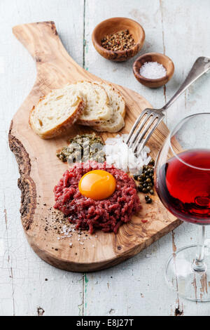 Beef tartare with capers and fresh onion on olive wood board with wine Stock Photo