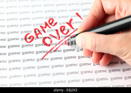 Woman's hand with red pen writing word "Game over" on the background of words "game". Stock Photo
