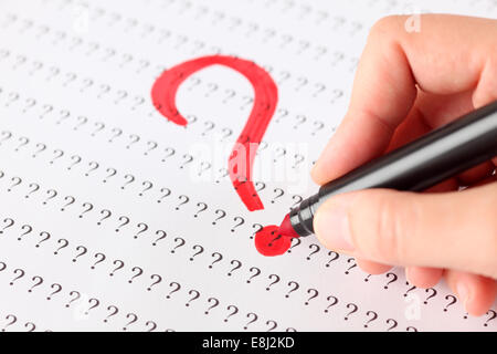 Woman's hand with red pen writing Question mark on the background of question marks. Stock Photo