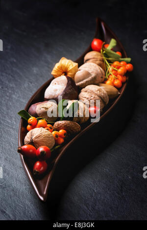 Decorative ceramic plate with nuts, berries and mushrooms over black background. Stock Photo