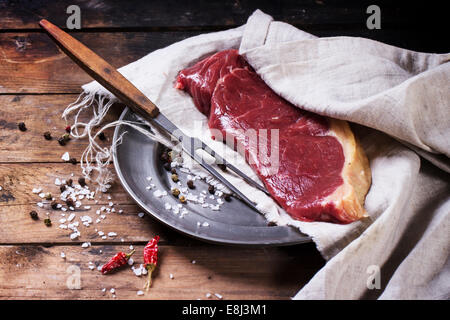 Raw steak on vintage metal plate over old wooden table. Stock Photo