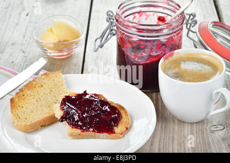Sweet breakfast with toasted bread, plum jam, butter and coffee on wooden table. Stock Photo