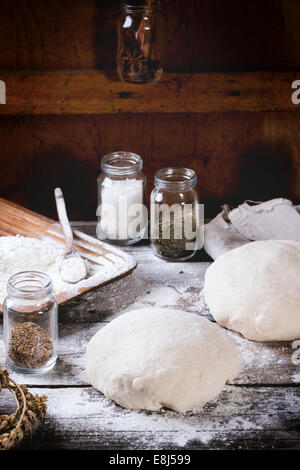 Baking bread. Dough on wooden table with flour, rolling-pin and jars with backing ingredients. Stock Photo