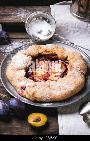 Galette cake with plums, served in vintage metal plate over old wooden table. Stock Photo