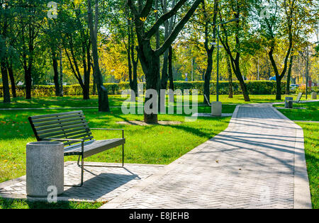 bench near the path of pavers in a quiet city park early autumn on a sunny day Stock Photo