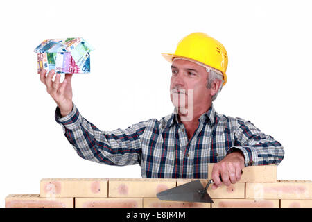 Builder with a house made of money Stock Photo