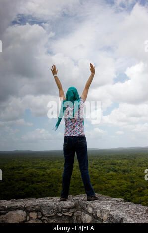 A woman open her arms above the jungle of top of a temple in the Mayan city of Calakmul, in Calakmul Biosphere Reserve, Campeche Stock Photo