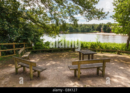 Shaded woodland lakeside picnic area with table and bench seats next to Rufford Lake at Rufford Abbey Country Park, Nottinghamshire, England, UK Stock Photo