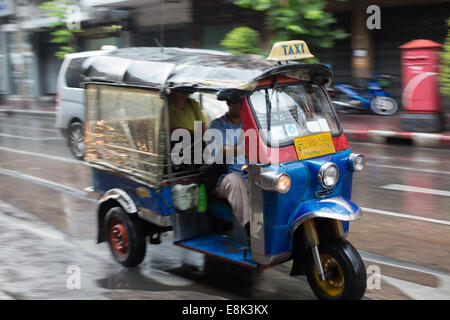 Tuk-tuk in blurred motion drives through a rainy Chinatown street, Bangkok, Thailand. Stock Photo