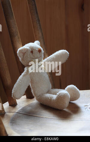 A small teddy bear is sitting on a wooden chair. Stock Photo