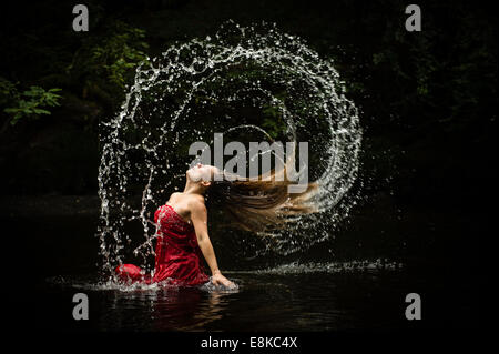 Fibonacci sequence: A blonde haired woman girl wearing a deep red frock ball gown in a river flicking flipping her hair Stock Photo