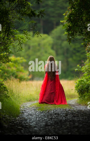 Scarlet woman: rear view back of a girl wearing a blood red frock dress stood standing alone in woodland countryside