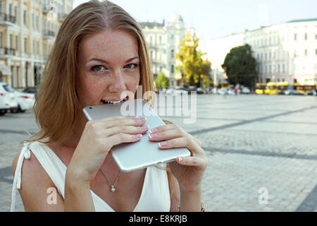 Young woman bite a tablet staying outdoor Stock Photo