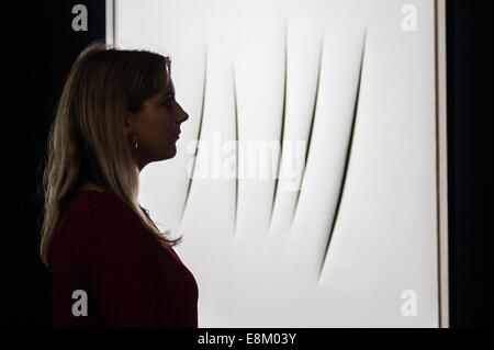 London, UK. 10th October, 2014.   a Sotheby’s assistant looks up at ‘‘Concetto Spaziale, Attese 1964’ by Lucio Fontana (Est. $2.2-2.8 million) during the press view of the Frieze week auction press view at Sotheby’s London. Credit:  Piero Cruciatti/Alamy Live News Stock Photo